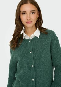 Zielony sweter z dzianiny o ribbowej fakturze, z przodem zapinanym na guziki ozdobionym perłowymi akcentami i klasycznym kołnierzykiem.