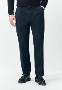 Dark gray tailored pants made of textured fabric, featuring pleats, a button closure, and a straight-leg design, paired with black shoes.