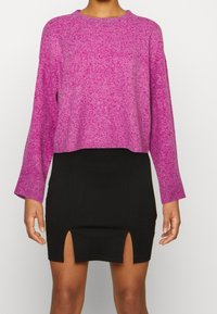 Maglione rosa macchiato con maniche lunghe e scollo rotondo, abbinato a una gonna nera aderente con una spaccatura frontale.