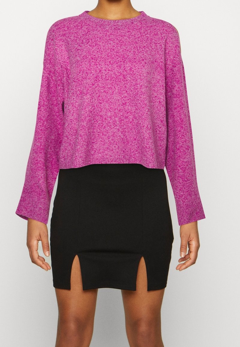 Maglione rosa macchiato con maniche lunghe e scollo rotondo, abbinato a una gonna nera aderente con una spaccatura frontale.