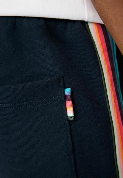 Námornomodré tepláky majú mäkkú textúru, bočnú kapsu a farebný prúžok pozdĺž boku v odtieňoch ružovej, oranžovej a zelenej.