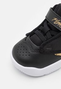 Černá sportovní bota s texturovaným síťovaným svrškem, hladkými koženými akcenty, perforovanou špičkou a bílou gumovou podrážkou. Obsahuje suchý zip.