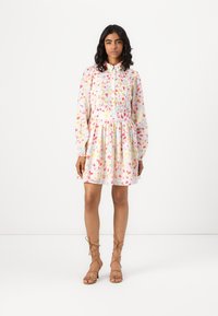 Λουλουδάτο φόρεμα με άσπρη βάση, ροζ και κίτρινες σχέσεις, σμιγμένο μπούστο, μακριά μανίκια και αέρινη φούστα. Φοριέται με σαγιονάρες σε καφέ απόχρωση.