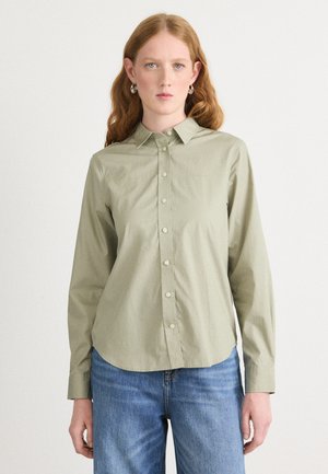 Camicia verde oliva chiaro con collo a punta, maniche lunghe e orlo arrotondato. Tessuto morbido, con apertura frontale a bottoni visibile e dettagli ai polsini.