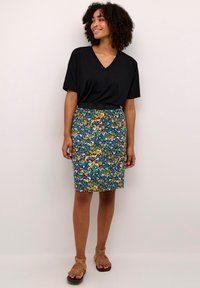 Camiseta negra de cuello en V, falda lápiz de longitud a la rodilla con estampado floral en azul, verde y naranja. Textura suave, cinturilla elástica, combinada con sandalias color tostado.