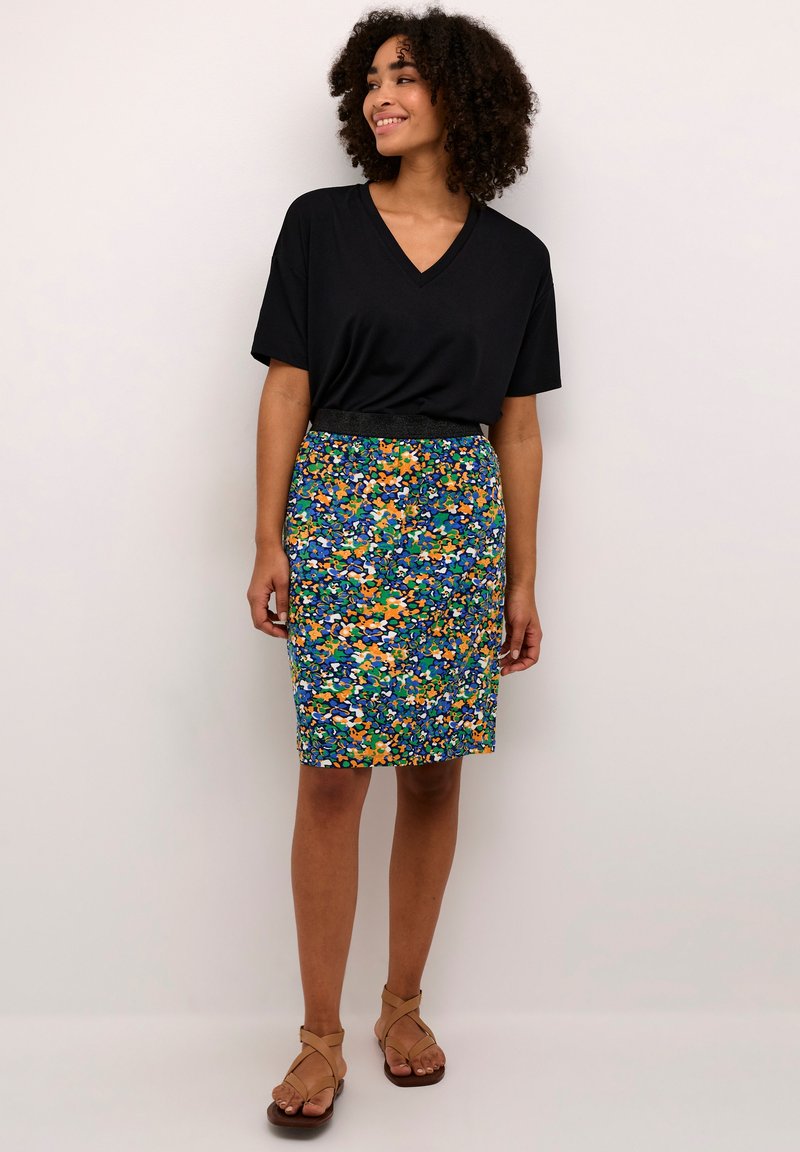 Camiseta negra de cuello en V, falda lápiz de longitud a la rodilla con estampado floral en azul, verde y naranja. Textura suave, cinturilla elástica, combinada con sandalias color tostado.