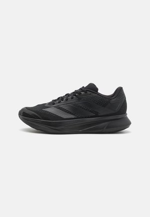 Scarpa atletica nera con materiali in rete e sintetici, design aerodinamico, suola curva e dettagli testurizzati sulla parte superiore.