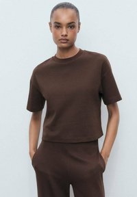 Brown short-sleeve cropped t-shirt in soft fabric with a round neckline. Model features a smooth texture and relaxed fit paired with matching pants.