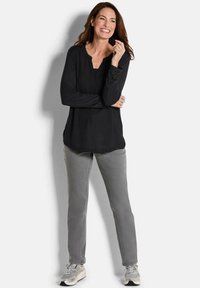 Top nero a maniche lunghe con scollo rotondo, abbinato a pantaloni dritti grigi chiari. Il modello indossa sneakers grigie con suola bianca.