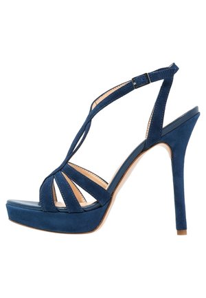 Granatowy zamszowy sandał na wysokim obcasie z platformą, odkrytymi palcami i wzorem pasków krzyżujących się na stopie oraz regulowaną klamrą na kostkę.