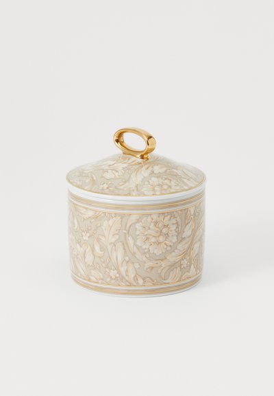 Porcelāna trauks ar ziedu reljefa rakstu bēšā un zeltā. Tam ir gluda tekstūra un zelta cilpas rokturis uz vāka.