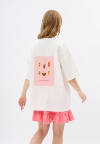 Witte oversized t-shirt met een roze graphic met illustraties van ijsjes en desserts, gecombineerd met een roze rok met ruches aan de onderkant.