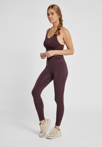 Donkerrode sporttanktop en legging met een geribbelde textuur, gecombineerd met lichtgekleurde sneakers met golvende accenten.