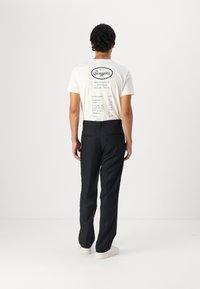 White t-shirt with a black graphic print listing menu items on the back, paired with black trousers and light-colored sneakers.