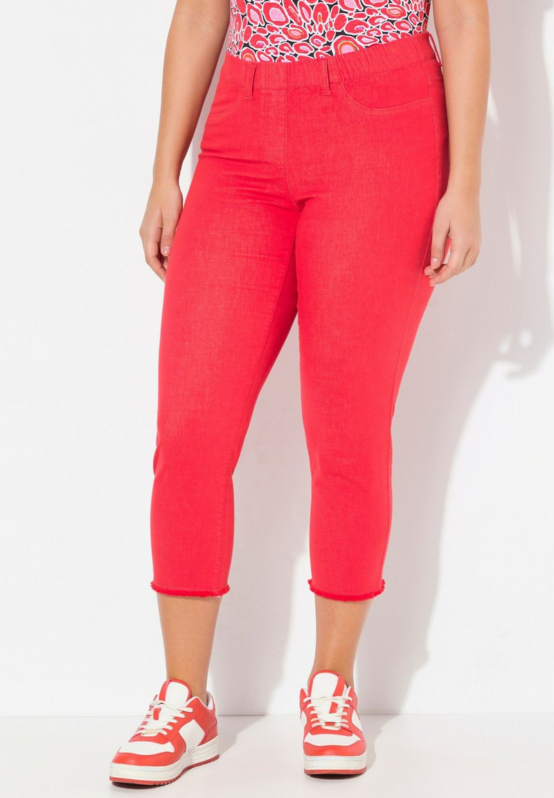 Röda avklippta jeans med en ljus denimstruktur, med en figursydd design och fransade fållar, kombinerade med röda och vita sneakers.