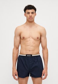 Navy blue boxer shorts made of lightweight fabric with a gray and black elastic waistband featuring the "BOSS" logo; button front detail.