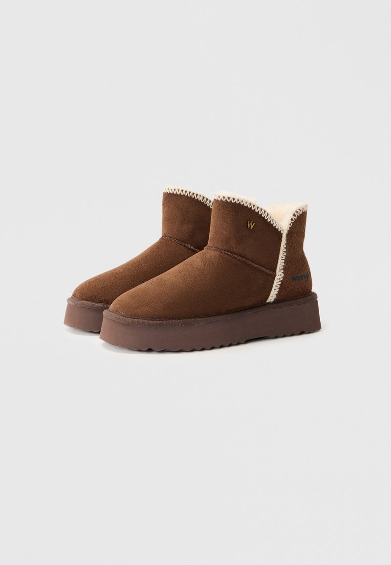 Stivaletti ankle in suede marrone con una fodera in pelliccia sintetica e una suola in gomma testurizzata. Presentano cuciture a contrasto e un piccolo logo sul lato.