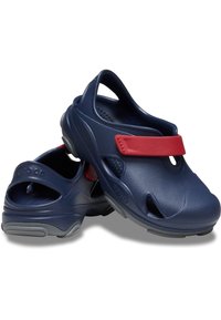 Clogs blu navy realizzati in materiale sintetico, con sezioni ritagliate, una cinghia regolabile rossa e suole testurizzate per una buona aderenza.