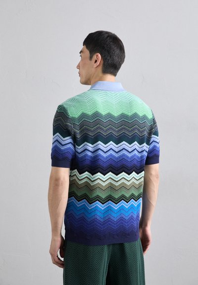 Polo cu mânecă scurtă, cu un model în zigzag în nuanțe de verde, albastru și marine, cu un guler bleo deschis și tiv elastic.