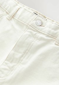 Weiße Denim-Jeans mit einem Reißverschluss und Knopfverschluss, sichtbaren Nähten und einer glatten Textur. Nieten-Detail am Bund.