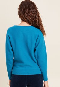 Blauer, weicher Strickpullover mit lockerer Passform, weitem Ausschnitt und geripptem Saum. Lange Ärmel und strukturierter Stoff. Sieht bequem und lässig aus.