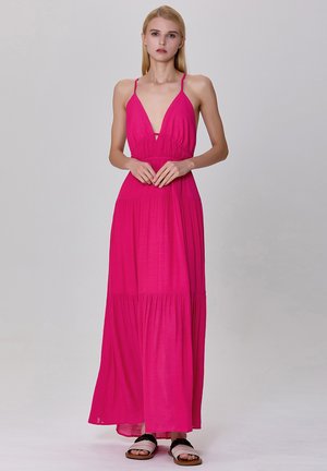 Robe maxi sans manches rose avec un décolleté en V profond, taille froncée et jupe à volants. Tissu léger avec un design fluide. Sandales plates.