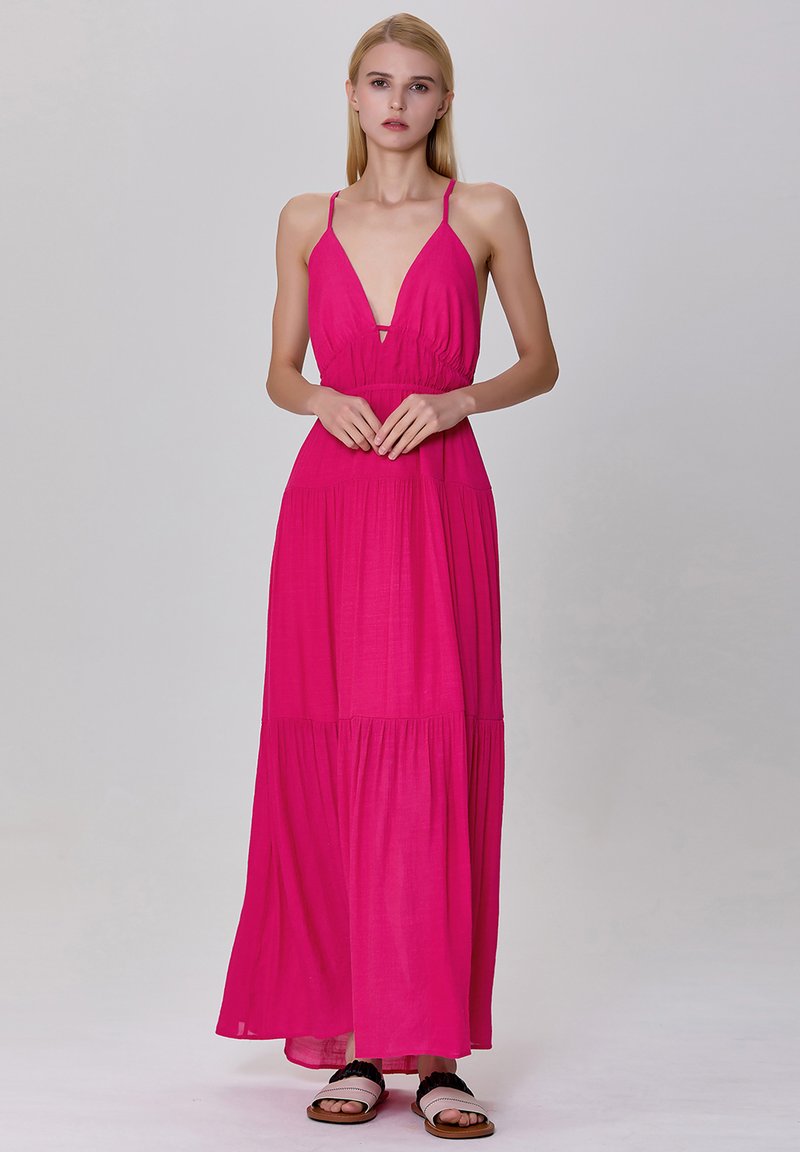 Robe maxi sans manches rose avec un décolleté en V profond, taille froncée et jupe à volants. Tissu léger avec un design fluide. Sandales plates.