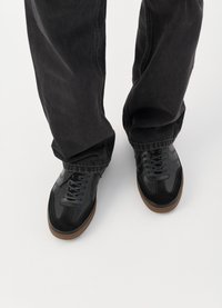 Melnas sporta kurpes ar gludu ādas virsmu, aprīkotas ar auklām un gumijas zoli. Valkātas ar brīvi pieguļošām melnām džinsu biksēm.