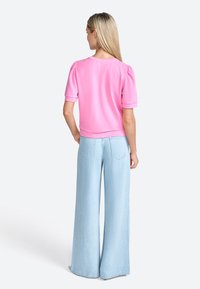 Top rosa a maniche corte con scollo rotondo e maniche a palloncino arricciate, abbinato a jeans a gamba larga blu chiaro con dettagli delle tasche posteriori.