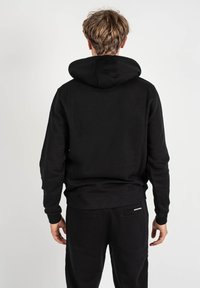 Sudadera negra con capucha ajustable, puños acanalados y dobladillo. Textura de tela suave; sin logos ni patrones visibles. Vista trasera.