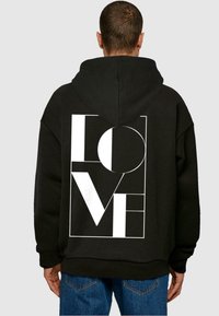Čierna mikina s kapucňou vyrobená z fleecového materiálu, s veľkým bielym grafickým nápisom "LOVE" na chrbte, doplnená geometrickými prvkami a kapucňou.