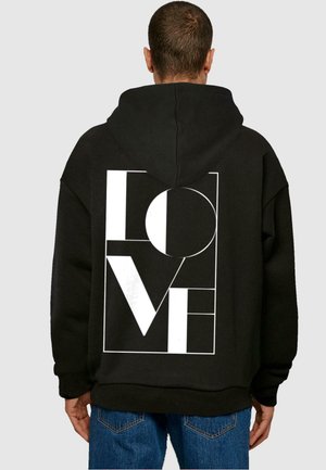 Sort hættejakke lavet af fleece-materiale, med et stort hvidt graphic, der skriver "LOVE" på ryggen, med geometriske elementer og hætte.