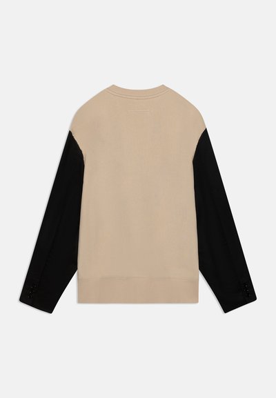 Beige stickad tröja med svarta långa ärmar. Har rund hals, ribbad nederkant och knappdetaljer på ärmarnas muddar.