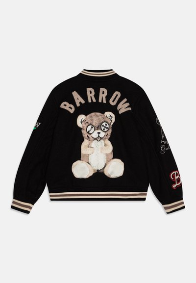 Mustvalge varsity jakk, mille seljal on tikitud pehme karu ja sõna "BARROW" selle kohal. Beezid soonikkoes mansetid ja ääred.