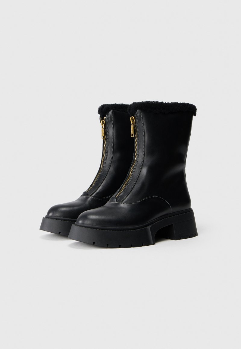 Zwarte leren enkellaarsjes met een faux fur manchet, gouden ritsdetails, stevige zool en een gladde afwerking. Dubbele ritssluiting.