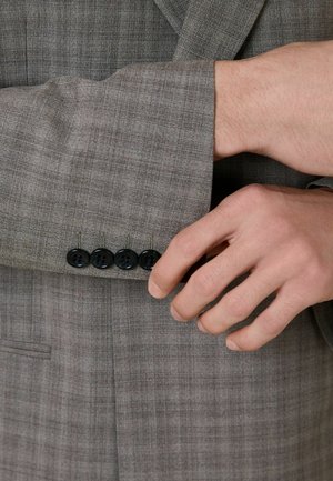 Hand stellt die Manschette eines grauen karierten Anzugsakts mit vier schwarzen Knöpfen ein.