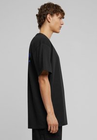 Sort bomulds T-shirt med korte ærmer, afslappet pasform, med blåt teksttryk på venstre ærme og rund halsudskæring.