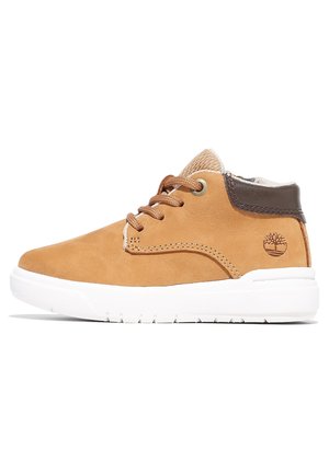 Baskets montantes en daim beige avec col marron, semelle en caoutchouc blanche, lacets à l'avant et logo arbre sur le côté du talon.