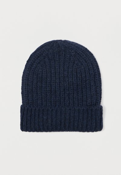 Donker marineblauwe gebreide wollen beanie met een omgeslagen rand, plat weergegeven op een lichte effen achtergrond.