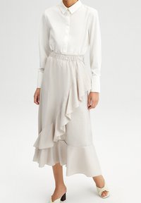 Camisa blanca ligera con botones combinada con una falda beige fluida que presenta volantes en capas y una cintura elástica.