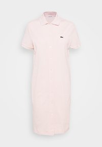 Polo dress in light pink cotton with a button front, short sleeves, and a small green logo on the left chest. Smooth texture, knee-length.