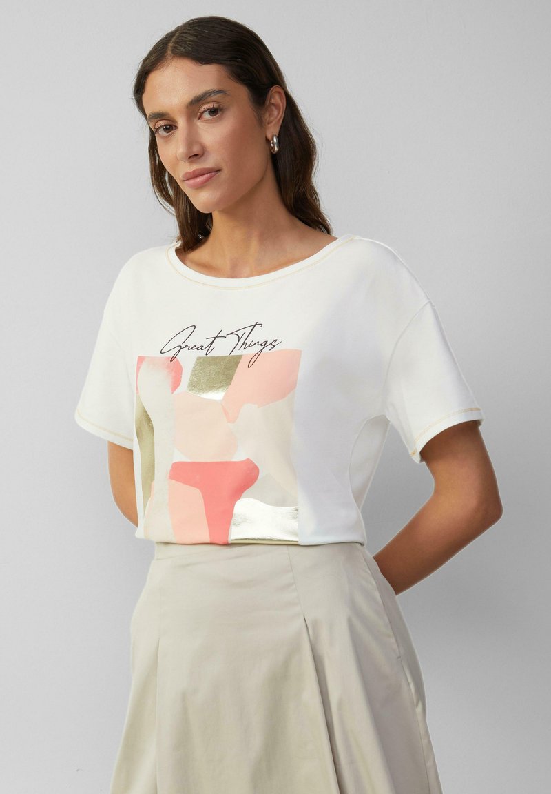 Witte T-shirt met korte mouwen, versierd met een kleurrijke abstracte print in tinten roze, gouden accenten en de tekst "Great Things" in cursief.