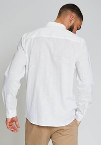 Camisa blanca de manga larga hecha de tela texturizada, con un cuello clásico y puños abotonados, con dobladillo recto y diseño de yugo trasero.