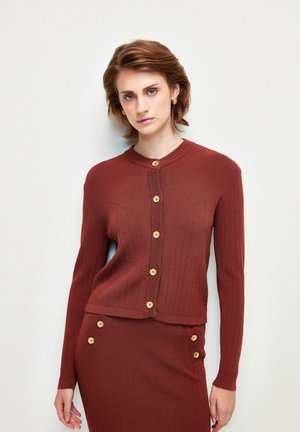 Rippstrickjacke in rostfarben mit langen Ärmeln, rundem Ausschnitt und Holzknöpfen auf der Vorderseite. Weicher Stoff, taillierte Passform.