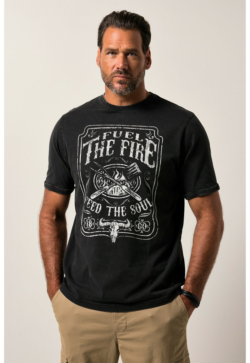 Camiseta negra de algodón con un diseño gráfico blanco que incluye el texto "ALIMENTA EL FUEGO, NUTRE EL ALMA" y una ilustración de una calavera de toro. Manga corta.