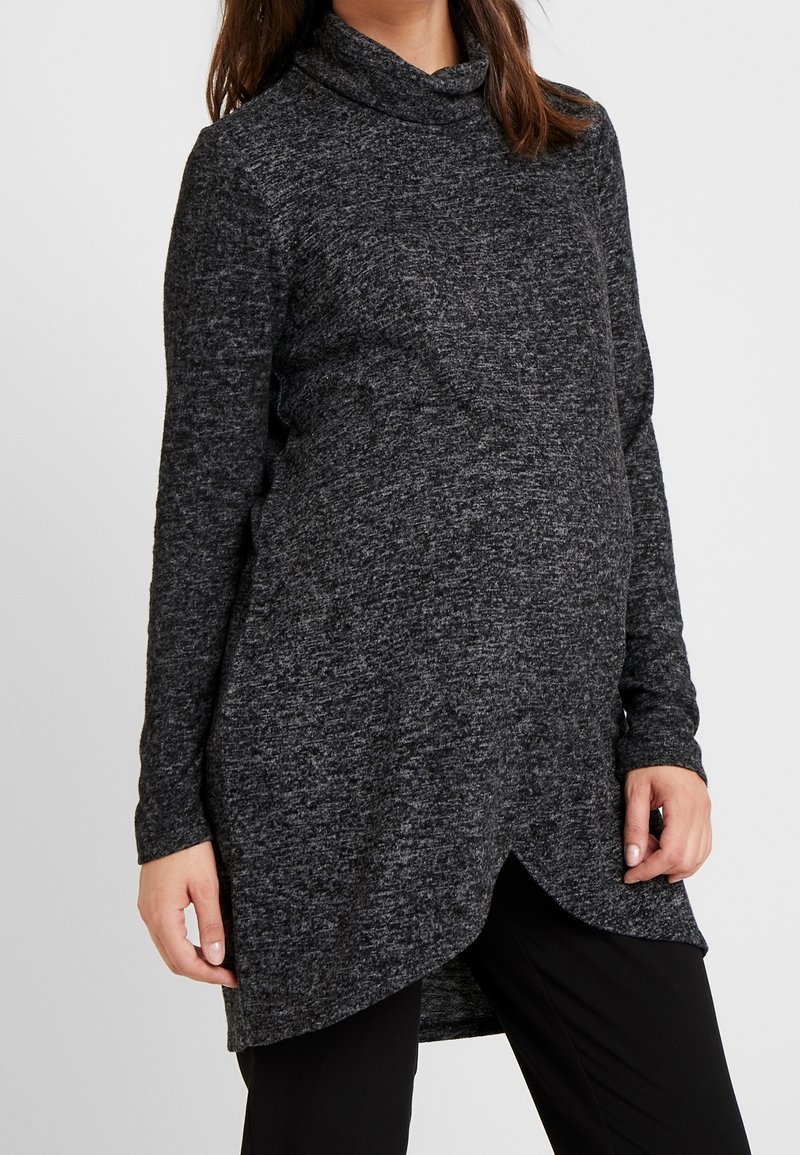 Schwarz und grau melierter Langarm-Tunika mit Schalkragen, asymmetrischem Saum und weichem Stricktextil, getragen über schwarzen Hosen.