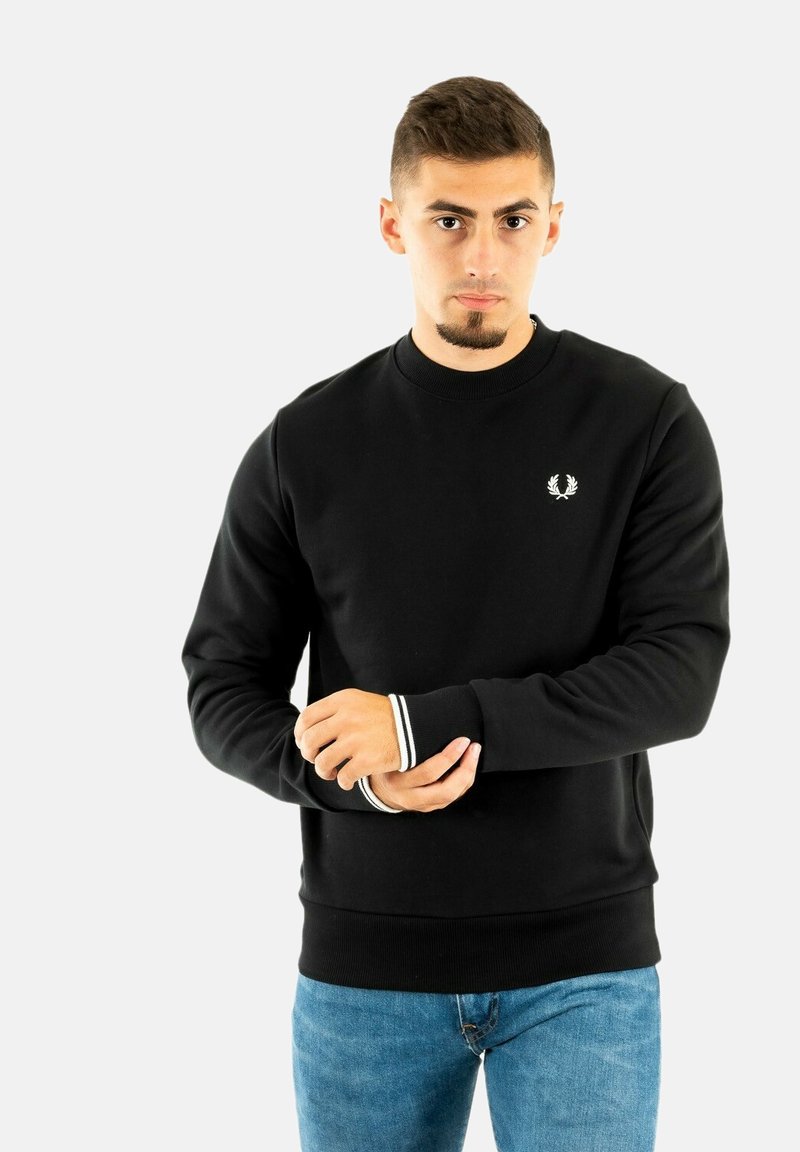 Sudadera negra con puños de canalé, que presenta un pequeño logo en el pecho y rayas blancas en contraste en las mangas. Textura de tela suave.