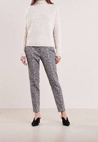 Pull en maille crème avec un motif texturé, associé à un pantalon noir et blanc à motif. Des talons noirs complètent la tenue.