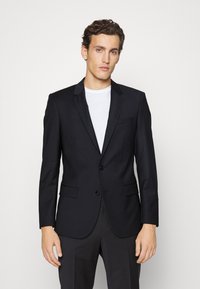 Zwarte op maat gemaakte blazer met twee knopen, gelapte revers, één borstzak en twee zijzakken. Glad stof met een moderne pasvorm.