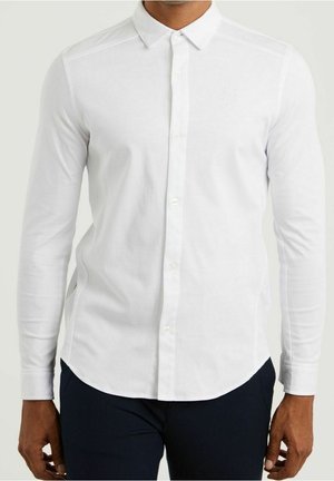 Witte overhemd met lange mouwen en knopen, voorzien van een klassieke kraag, een gladde textuur en subtiele borduursels op de borst. Gekleed met donkere broek.